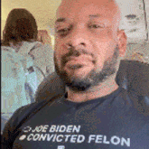 a man with a beard is wearing a t-shirt that says `` biden convicted felon '' .