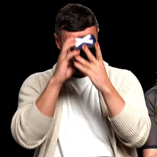 a man wearing a white shirt and a tan sweater is covering his eyes with his hands