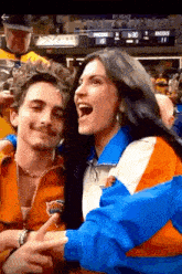 a man and a woman are posing for a picture in front of a scoreboard that says knicks