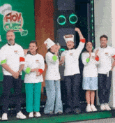 a group of chefs are standing on a stage in front of a green background .