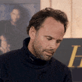 a man in a turtleneck sweater stands in front of a sign that says honorelli