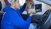 a man in a blue hoodie is taking a taco bell bag out of a drive thru window