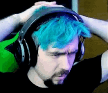 a man with blue hair is wearing headphones and has his hands on his head