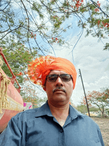 a man wearing an orange turban and sunglasses stands in front of trees