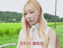 a woman with long blonde hair is sitting in a field with a sign that says ' oii ' on it
