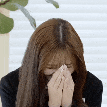 a woman covering her face with her hands and a plant in the background