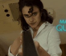 a woman in a white shirt is holding a gun in front of a neon sign that says " ma que "