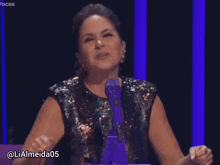 a woman in a sequined top stands in front of a microphone with the hashtag lialmeida05 on the bottom