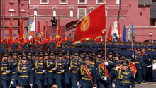 a group of soldiers marching in front of a building with a picture of a man on it