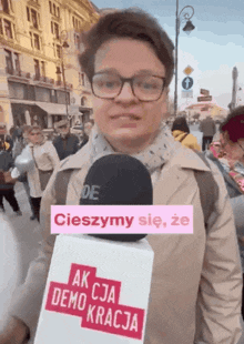 a woman wearing glasses is holding a microphone with a sticker that says akcja demokracja