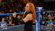 a woman is standing in a wrestling ring with her arms crossed and a crowd watching .