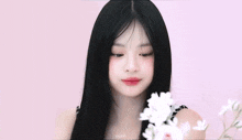 a girl with long black hair is holding a white flower in her hand and pointing at it .