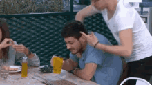 a man is sitting at a table with a glass of orange juice and a woman is standing behind him .