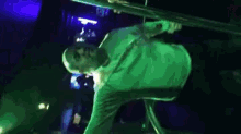 a man in a green shirt is standing upside down in a dark room with a blue light behind him .