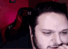 a man with a beard is sitting in a red chair and looking at the camera .