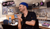 a man wearing a blue hat stands in front of a sign that says k-eth 101.1