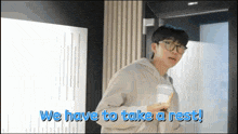 a man with glasses holds a cup of coffee and says we have to take a rest !