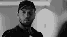 a black and white photo of a man with a beard wearing a hat .