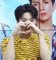 a young man in a yellow and black striped shirt is making a heart with his hands .