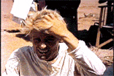 a man wearing a white shirt is scratching his head