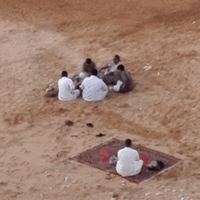 a group of people are sitting on a mat in the sand