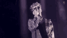 a man wearing sunglasses and a plaid shirt is holding a microphone and singing into it .