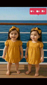 two little girls wearing yellow dresses are standing next to each other on a deck