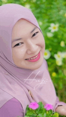 a woman wearing a purple hijab smiles while holding flowers