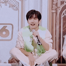 a young man sitting on the floor holding a microphone with the number 6 in the background