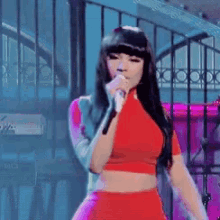 a woman singing into a microphone while wearing a red crop top and pink skirt