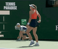 a tennis player stands on a tennis court in front of a sign that says tennis paradise