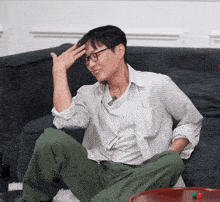 a man with glasses sits on a couch with his hand on his forehead