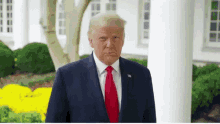 donald trump in a blue suit and red tie stands in front of a white house