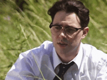 a man wearing glasses and a tie sits in a field