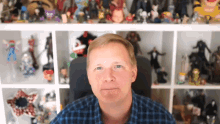 a man in a plaid shirt is sitting in front of a shelf full of toys