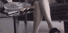 a woman is sitting on a couch with her legs crossed next to a table with a gun and an ashtray .