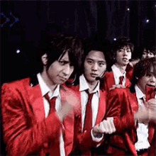 a group of young men in red suits and ties are clapping .
