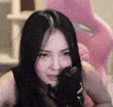 a woman with long black hair is sitting in front of a pink chair holding a microphone .