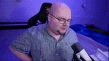 a bald man wearing glasses is sitting in front of a microphone .