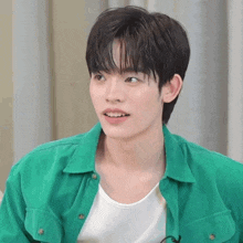 a young man wearing a green shirt and a white tank top smiles