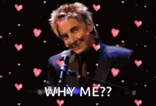 a man in a suit is singing into a microphone and the words why me are surrounded by hearts .