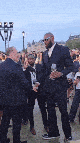 a man in a suit holds a glass of wine and shakes hands with another man