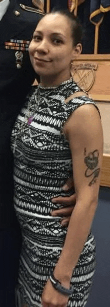 a woman in a black and white dress with a tattoo on her arm is standing next to a man in a military uniform .