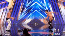 a couple of men are dancing on a stage with a nbc logo in the background