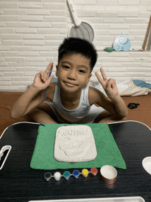 a young boy sits at a table with a piece of clay that says ' a ' on it