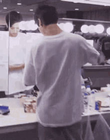 a man in a gray shirt is standing in front of a mirror .