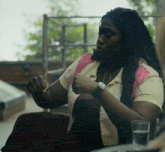 a woman wearing a watch sits at a table with a glass of water in front of her