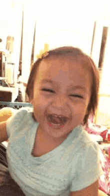 a little girl in a blue shirt is smiling with her mouth wide open