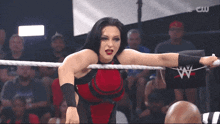 a woman in a red and black outfit is standing in a wrestling ring with a cw logo in the background