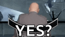 a bald man in a suit is sitting in front of a sign that says yes ?